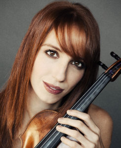 Catherine Cosby in a black dress with long red hair holding her violin with gray background.