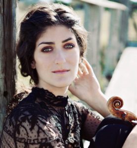 Michelle Ross with long black hair up, and black lace dress, seated with violin on her legs.