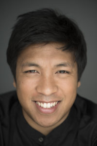 Yannick Rafalimanana in a black buttoned shirt and short black hair close up against a gray background.
