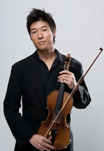 Charles Yang with spiky black hair in a black shirt/pants holding his violin in front of a light gray background.