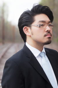 Euntaek Kim in dark suit with light blue tie and glasses standing on train tracks.