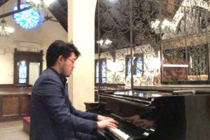 Euntaek Kim playing piano in a church with rose window at the back.