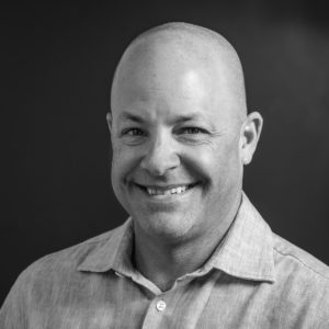 Black and white photo of Andrew Chmura in a collared shirt with a black background