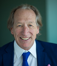 Photo of Dean Goodermote in a navy suit and tie with a green background