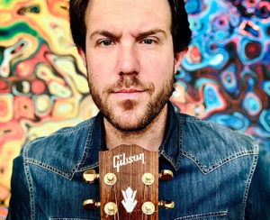 Portrait of Jason Spooner with Gibson guitar in front of street art