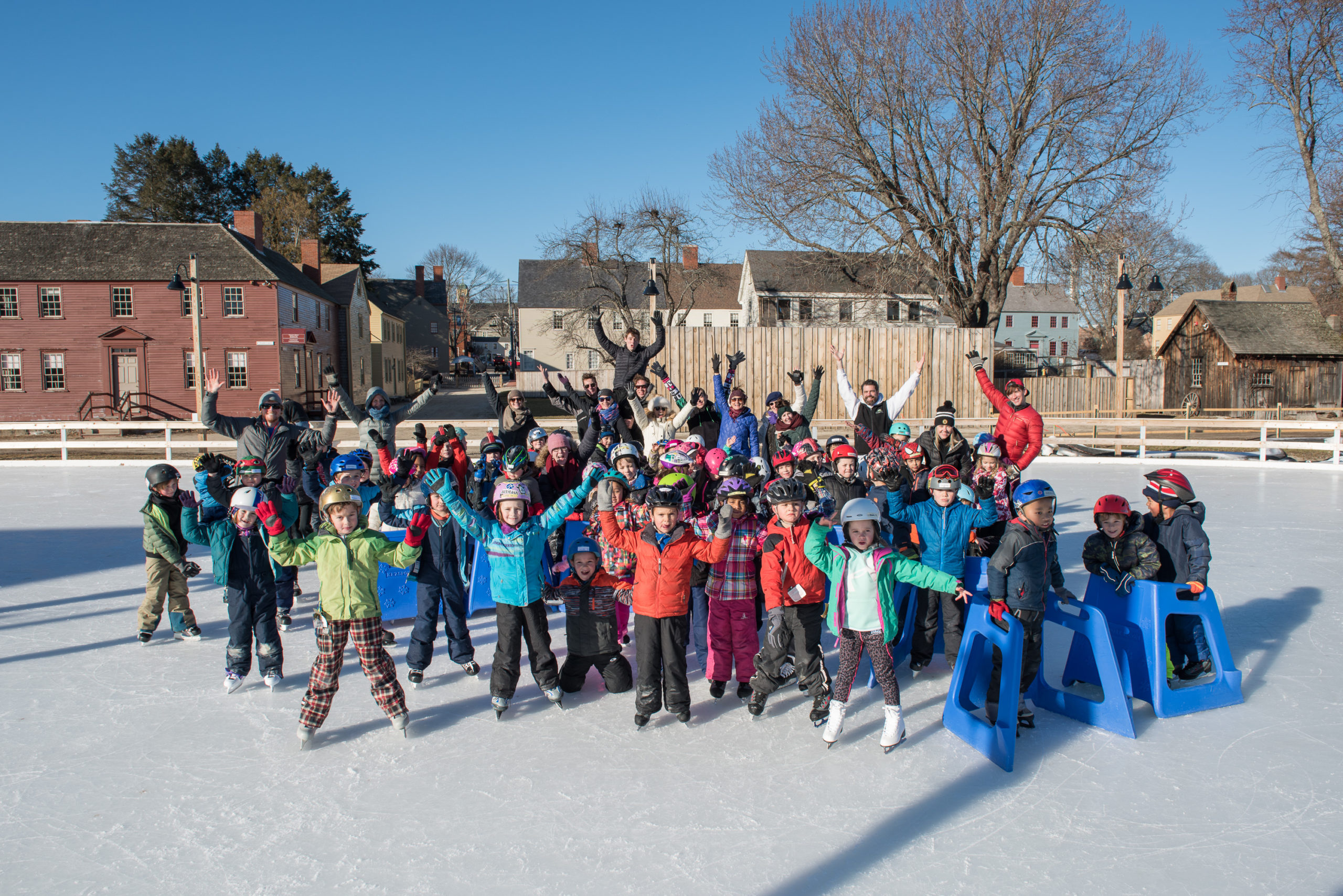 A group of brightly dressed skaters comprised of first grade students and the Ice Dance International Company pose together on the ice.