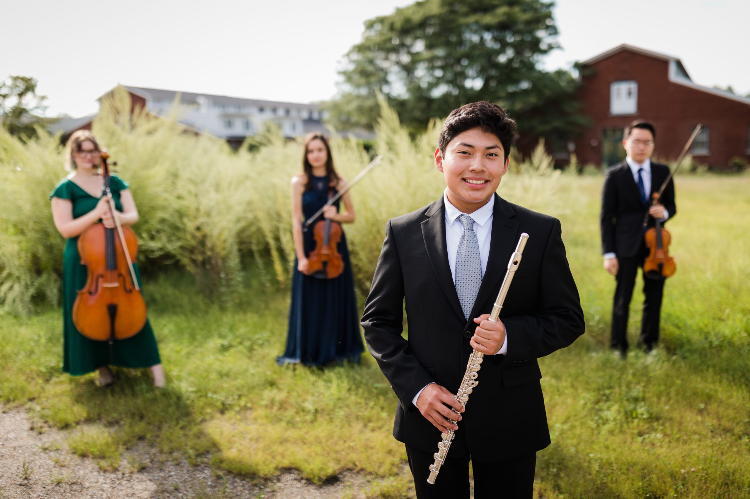 teenagers in a field holding musical instruemnts hightlighted is a young man holding a flute