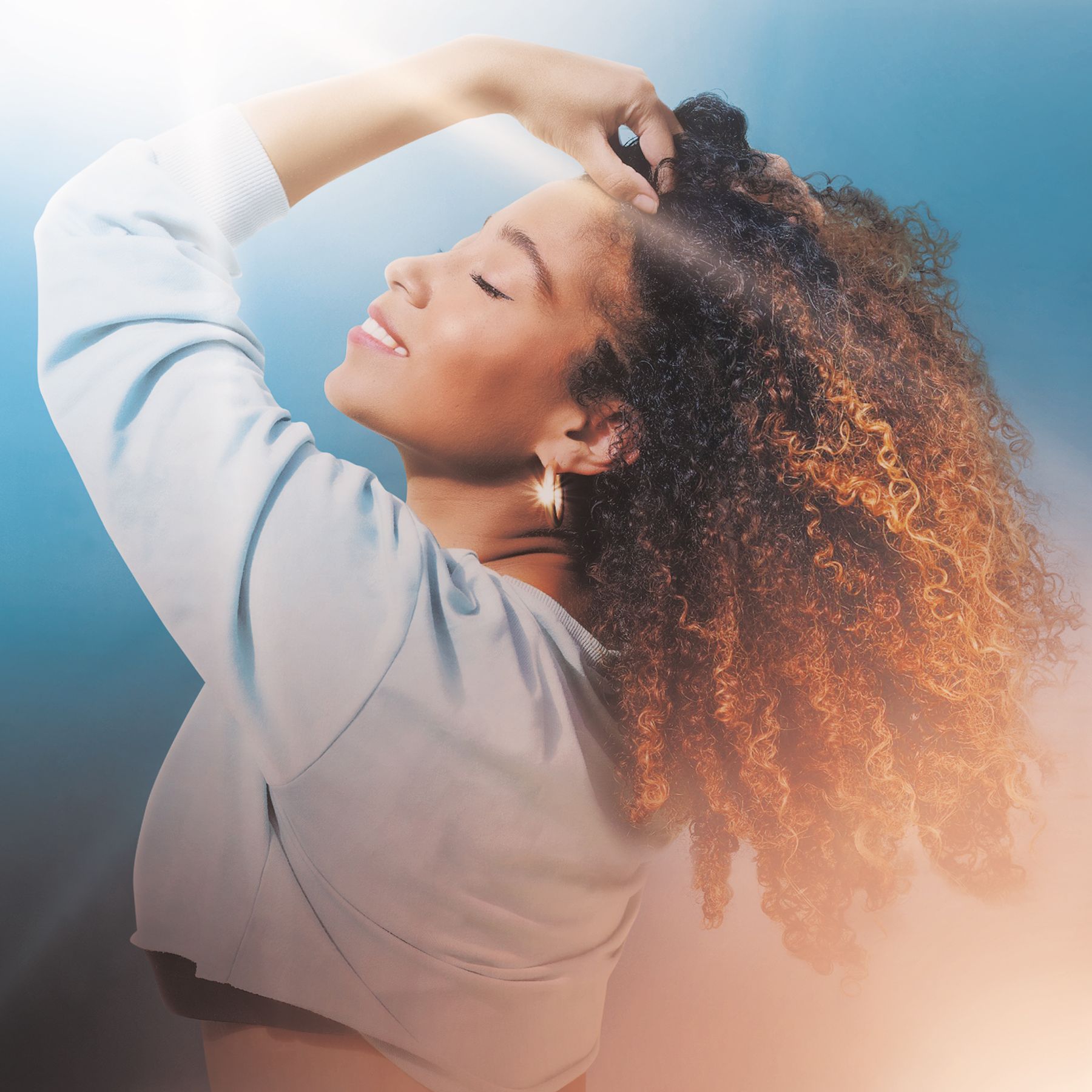 Image of Singer Myra Flynn- wearing a light blue long sleeve shirt. She is standing with her left arm bent toward her head with light streaks in the top left and bottom right corners of the image.